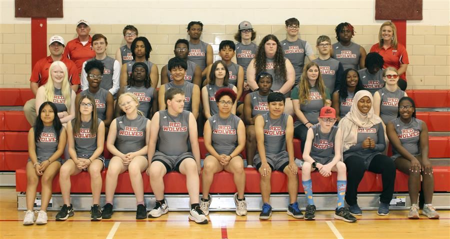  A track team group photo with members wearing gray uniforms and standing on gym bleachers.